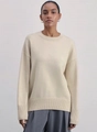 Detail of ribbed knit cuffs and hem on a loose beige crewneck sweater with drop shoulders - Apricot