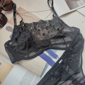 Detalle de un sujetador de encaje negro con bordado floral y etiqueta sobre una base blanca - Negro