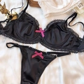 Completo intimo in raso nero e pizzo con fiocchi rosa su sfondo di seta morbida - S / Nero