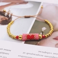 Detail of handmade Miyuki heart bracelet with gold beads and adjustable cord on a magazine - Pink