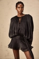 Detail of black pleated fabric dress featuring lantern sleeves and wavy hem design - Black