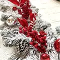 Ghirlanda natalizia innevata con bacche rosse, pigne e decorazioni su parete bianca - Festone Fioccato Rosso / Stile Corto