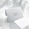 White jewelry polishing cloth with jagged edges and elegant pearlescent paper packaging - White