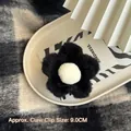Gros plan d'une pince à cheveux fleur en peluche de 9 cm en noir et blanc sur plateau - Noir