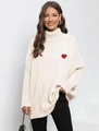 Dettaglio del ricamo a cuore rosso su un maglione a dolcevita oversize color crema - Taglia unica / Albicocca