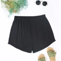 Flat lay of black ribbed beach shorts with summer sunglasses and woven sandals on white - Ribbed Black