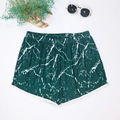 Detailed flat lay of green marble print beach shorts with white piping and summer props - Dark Green