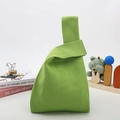 Detail view of avocado green knit handbag with cross-handle closure on a wooden desk - Yellow-Green