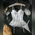 Flat lay of white lace bodysuit set with garter belt and corset lacing on black background - S / White