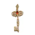 Close-up of golden vintage key pendant with red zircon and sparkling white stones - Red Gem Key Pendant