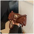 Macro view of polished brown leather shoulder bag with large silver buckle and side zipper - Brown