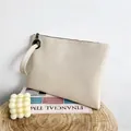 Ivoorwitte envelop clutch met hagedisreliëf, ritssluiting en polsband op houten voet - Broken Wit