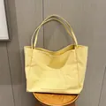 Minimalist light yellow canvas tote bag with front pocket displayed on a wooden stool - Yellow