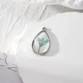 Vue macro du pendentif en résine goutte avec fleurs séchées bleues et cadre en métal argenté - Fleur Bleu Lac