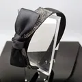 Detail of black satin headband featuring a crystal-encrusted bow on a clear acrylic stand - Black Satin Bow Headband with Mineral Gray Rhinestones
