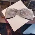 Macro shot of shimmering rhinestone bow hair clip with silver crystals on black fabric - White