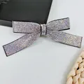 Detailed view of luxury bow hair clip featuring iridescent rhinestones on a black fabric base - Rainbow