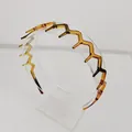 Macro view of amber wavy zigzag headband with anti-slip teeth on a clear display stand - Wide Teeth Style / Coffee