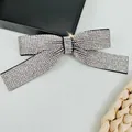 Macro detail of luxury silver rhinestone bow hair clip with central black ribbon accent - White