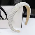 Detail of high-crown padded headband with AB crystals and pearls on beige suede lining - Straight Style / 2.5cm / AB Rhinestone / [product Attributes] This Product Is [visually] A Wide Thickened Sponge Headband Densely Inlaid With [illustrated] Ab-colored Iridescent Rhinestones And Miniature Imitation Pearls. The Lining Is [visually] Apricot-colored Suede-like Material Increasing Wearing Comfort And Friction. [visual Presentation] The Image Uses A Close-up Overhead Perspective. The Headband Is Arranged Diagonally Creating A Distinct Sense Of Layering. The Background Uses A White Shopping Bag And Black Ribbon To Create A Sense Of Sophistication With An Overall Bright And Pure Tone. Image Quality Is [high] With Accurate Focus. Aesthetic Appeal Is [high] With An Overall Score Of [8.5]. The Contrast Of Light And Shadow Effectively Highlights The Sparkling Texture Of The Rhinestones. [text Content] All Text Belongs To Prop_text Including The Remaining "anel" Brand Lettering On The Background Gift Bag And The Artistic English Poem At The Top. No Translation Or Removal Is Necessary. [logistics Labels] None [infringement Risk] The Product Itself Is A Generic Design Without Brand Logos With An Infringement Probability Of [0.1]. The Background Prop The Shopping Bag Involves [chanel - Shopping Bag - Brand Text]. 【product Parameters】product: Thickened Rhinestone Headband;material: Iridescent Rhinestones Imitation Pearls Fabric.