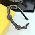 Detailed close-up of a twisted black headband with sparkling silver rhinestones on a yellow box - Transparent Grey Rhinestone