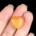 Pierre de cristal naturelle orange polie en forme de cœur entre les doigts - Jade Jaune