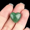 Polished heart-shaped green aventurine gemstone held in hand with black background - Green Aventurine