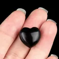 Polished black heart-shaped natural crystal stone held between fingers showing size - Obsidian