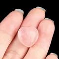 Polished natural rose quartz heart-shaped stone held by fingers for size reference - Rose Quartz