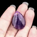 Hand holding a teardrop-shaped purple amethyst gemstone pendant with natural textures - Purple Crystal
