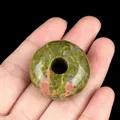 Green and pink unakite natural stone donut bead held in hand for scale with black background - Unakite