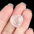 Hand holding a heart-shaped rose quartz stone with natural pink textures on black background - White Crystal