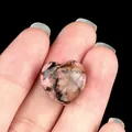 Pink rhodonite heart-shaped stone with black veins held between fingers - Rhodonite