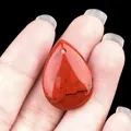 Polished red jasper teardrop pendant with natural black veins held in palm - Red Jasper