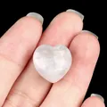 Polished heart-shaped natural white crystal stone held between fingers for size - Agate