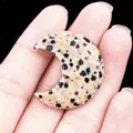 Pendentif lune de 30mm en jaspe dalmatien naturel tenu délicatement à la main - Pierre Tachetée