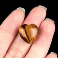 Polished natural tiger eye crystal heart stone held in hand for size comparison - Tiger's Eye
