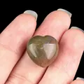 Polished heart-shaped natural agate stone in green and brown tones held in hand - India Agate