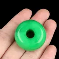 Vibrant emerald green agate donut bead pendant held up against a solid black background - Dyed Malaysian Jade