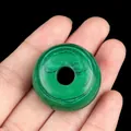 Natural malachite donut pendant with green banded patterns held in hand for size comparison - Malachite (Synthetic)