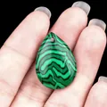 Teardrop-shaped green malachite pendant with black stripes held by hand - Malachite (Synthetic)