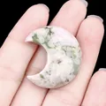 Pendentif lune en agate naturelle à texture verte tenu en main pour l'échelle - Jade de Bon Augure