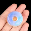 Handheld 30mm milky white opalite donut bead with a soft blue iridescent glow - Opal (Synthetic)