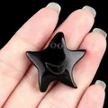 Polished black obsidian star ornament with a carved smiley face held in hand - Obsidian