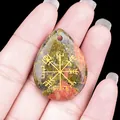 Colgante gota de unakita con símbolo brújula Vegvisir dorada sobre la palma de la mano - Unakita
