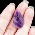 Faceted purple amethyst teardrop pendant held by hand showing natural texture - Amethyst