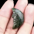 Carved natural green agate stone moon face pendant held by hand against black background - India Agate
