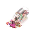Macro shot of colorful iridescent candy paper flakes spilling from a small 15ml glass bottle - Multicolor
