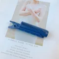 Close-up of a blue plastic hair root volumizing clip with fine comb teeth on a card - Blue