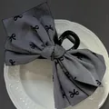 Dettaglio di una grande molletta per capelli in tessuto grigio con motivi di farfalle nere - Grigio